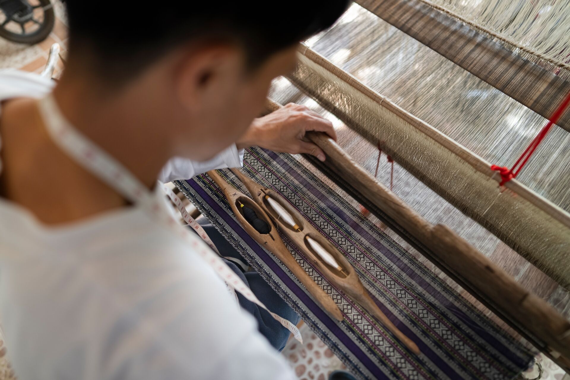 Young Asian man weaves native cloth from traditional wooden loom
